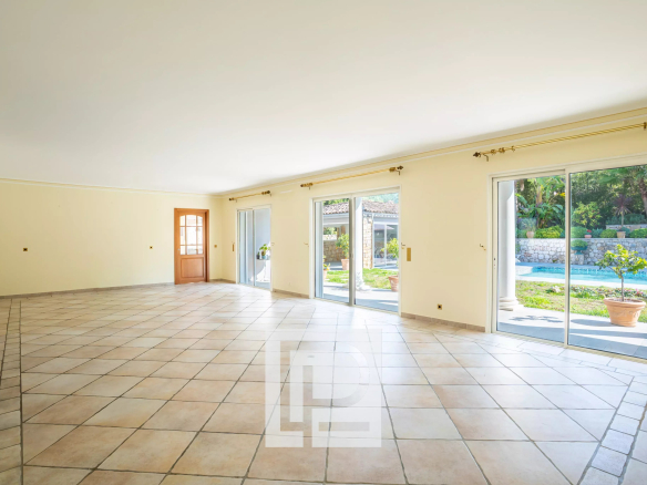 Bright empty living room with beige walls, tiled floor, and large sliding doors opening to a pool and patio outside.
