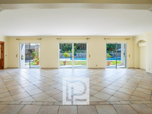 Bright empty living room with tiled floor and wide sliding glass doors opening to a garden and pool area outside.