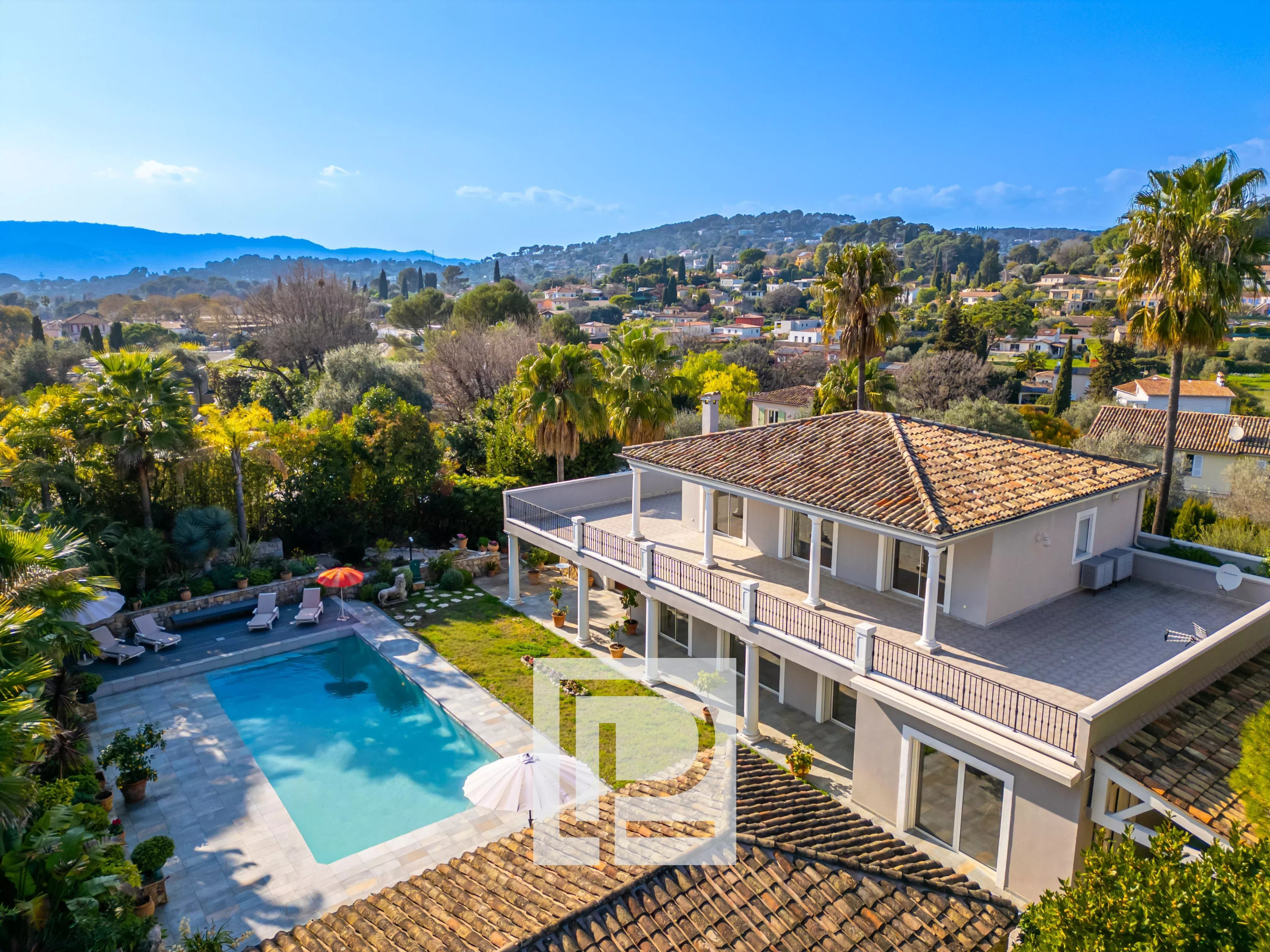 Aerial view of a two-story villa with a tiled red roof, spacious balcony, and a rectangular pool in a landscaped yard