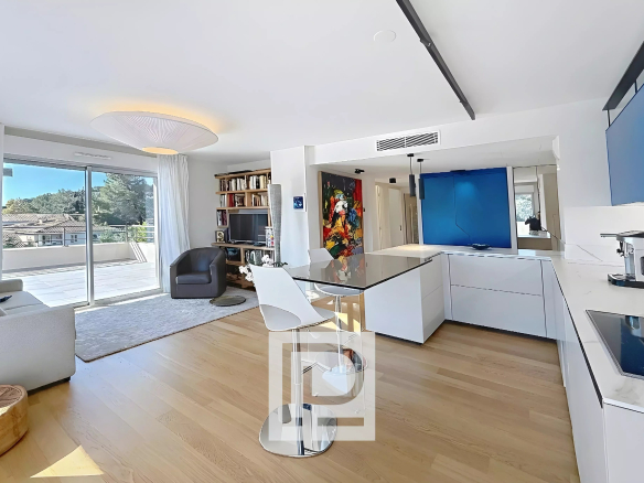 Bright open-plan kitchen and living area with white cabinets, glass-top island, and a blue feature wall by the hallway.