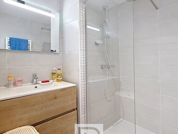 Modern bathroom with a glass-enclosed shower, rainfall head, white tiled walls, and a wooden vanity with sink.