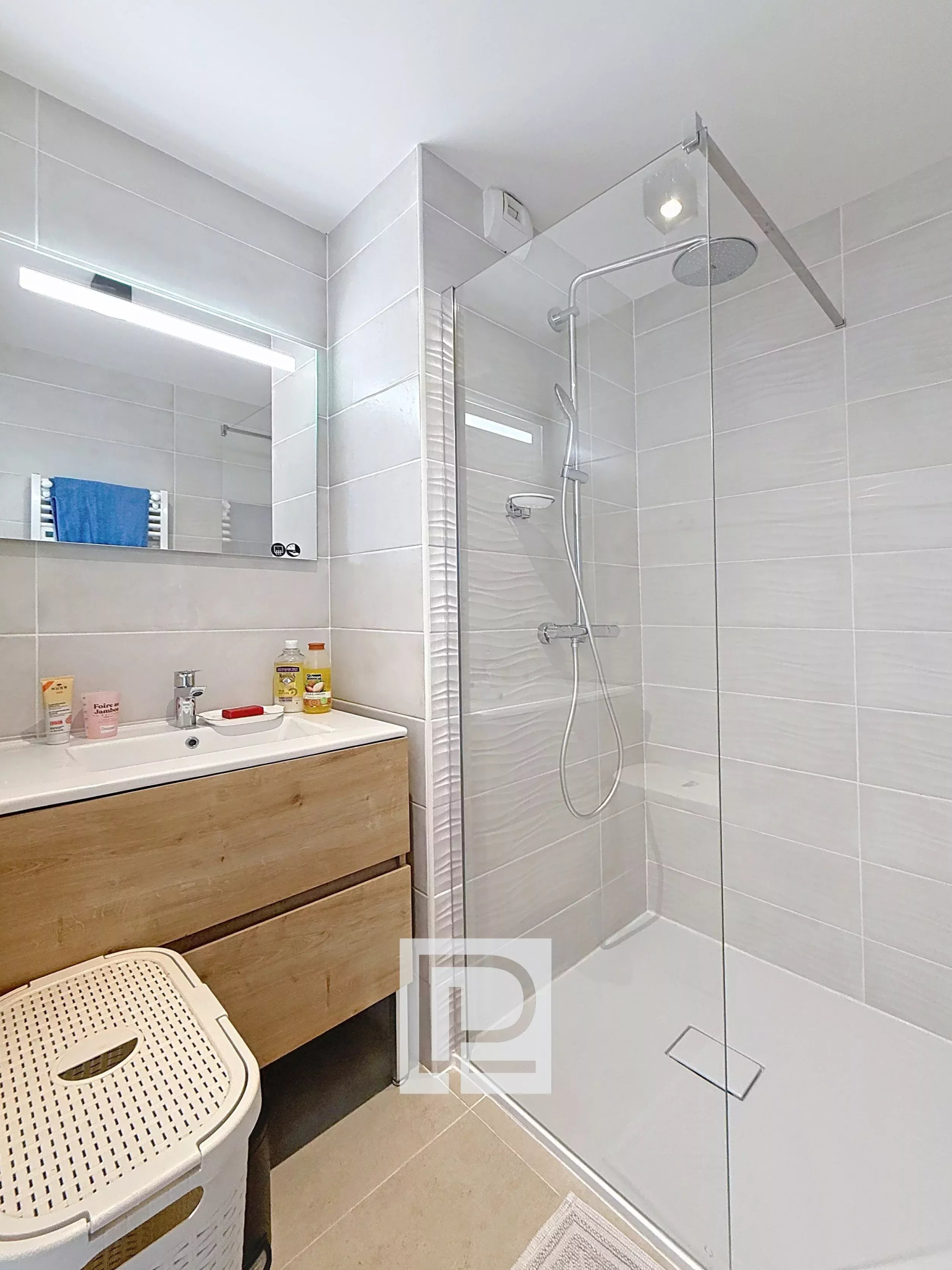 Modern bathroom with a glass-enclosed shower, rainfall head, white tiled walls, and a wooden vanity with sink.