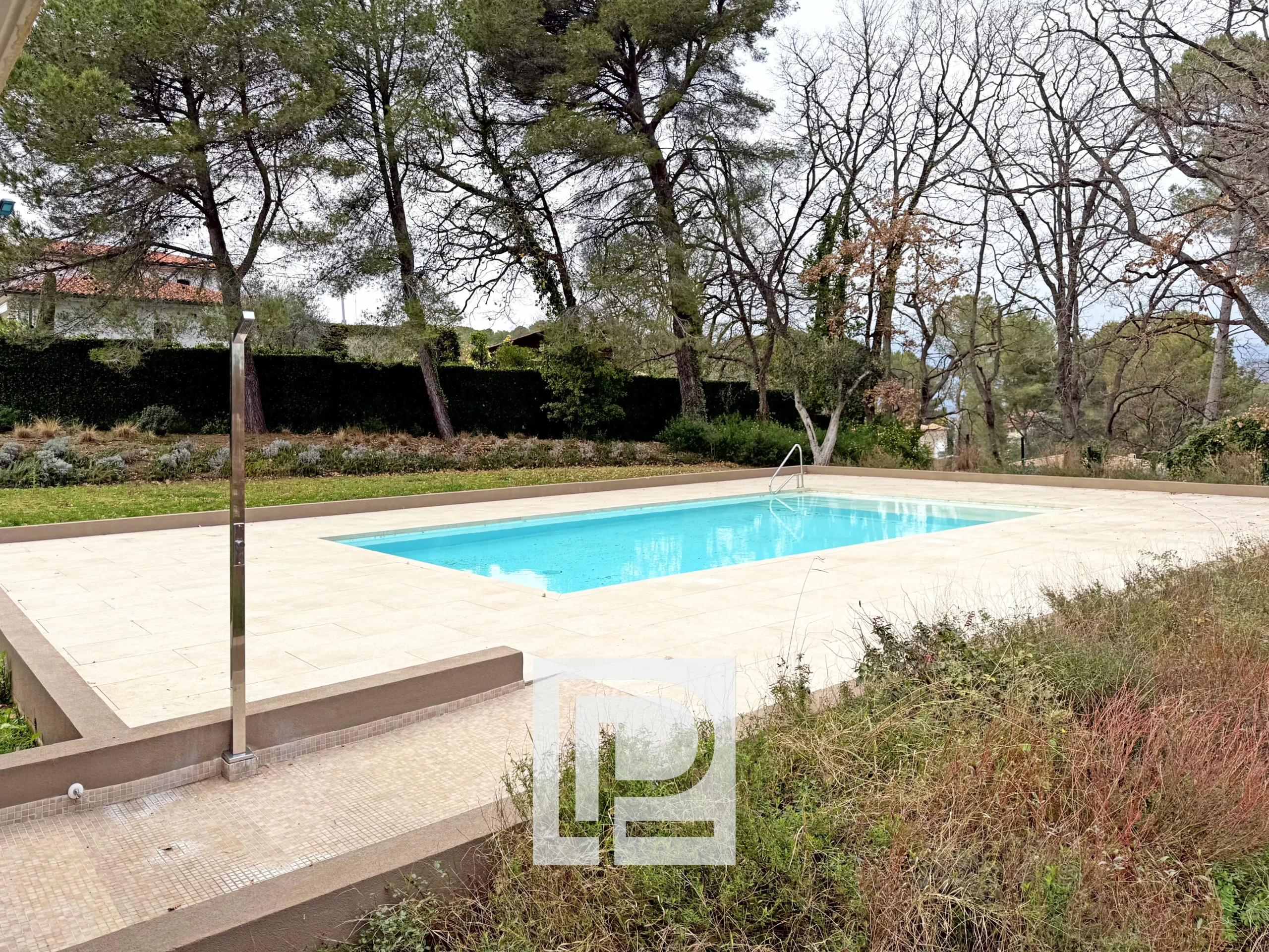 Outdoor rectangular swimming pool with turquoise water bordered by light beige tiles and trees in the background.