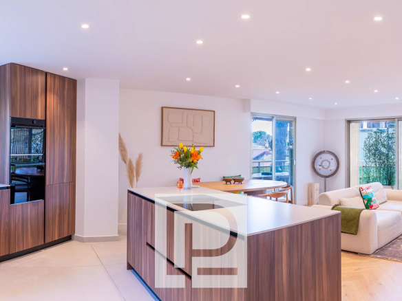 Open-plan kitchen and living room with dark wood cabinets, an island, and a beige sofa by large glass doors to outdoors.
