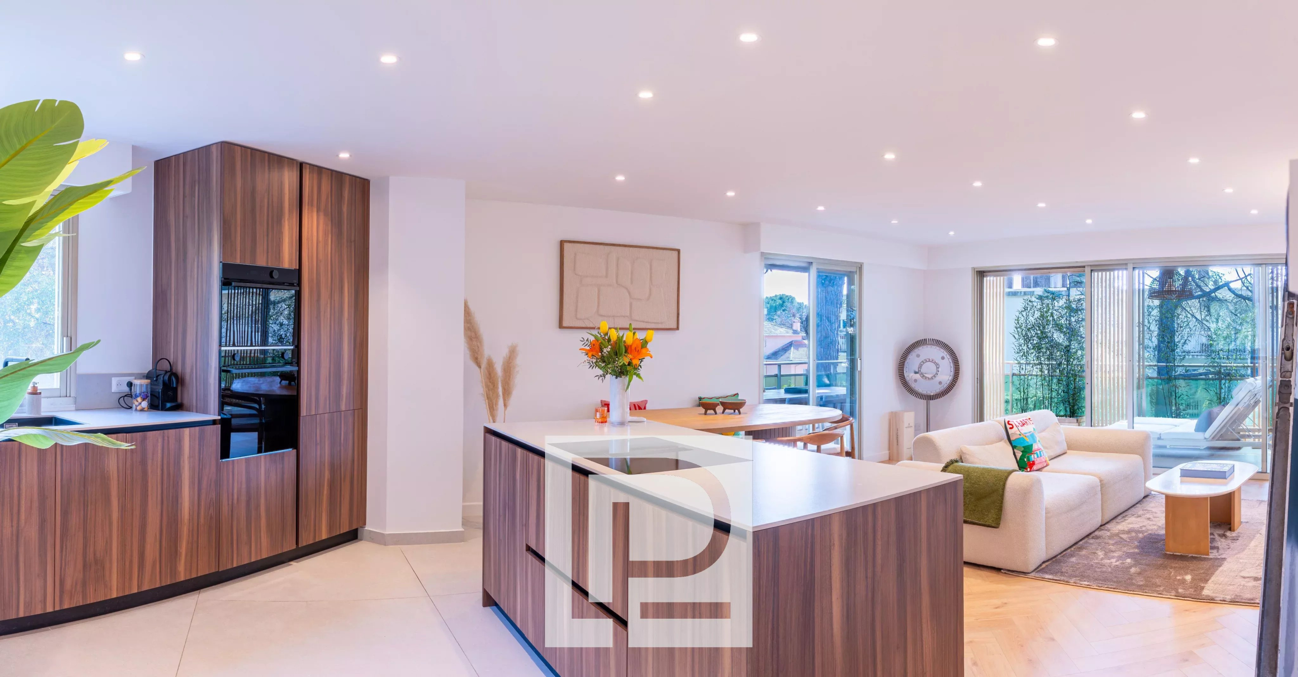 Open-plan kitchen and living room with dark wood cabinets, an island, and a beige sofa by large glass doors to outdoors.