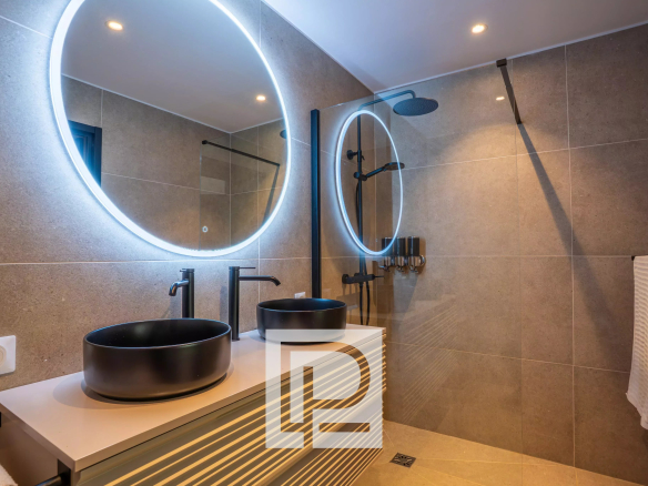 Modern bathroom with double black vessel sinks, backlit circular mirrors, and a glass shower.