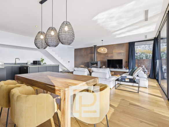 Open-plan living area with a wooden dining table and mustard chairs, grey kitchen cabinets, and a cozy lounge with a fireplace and TV.
