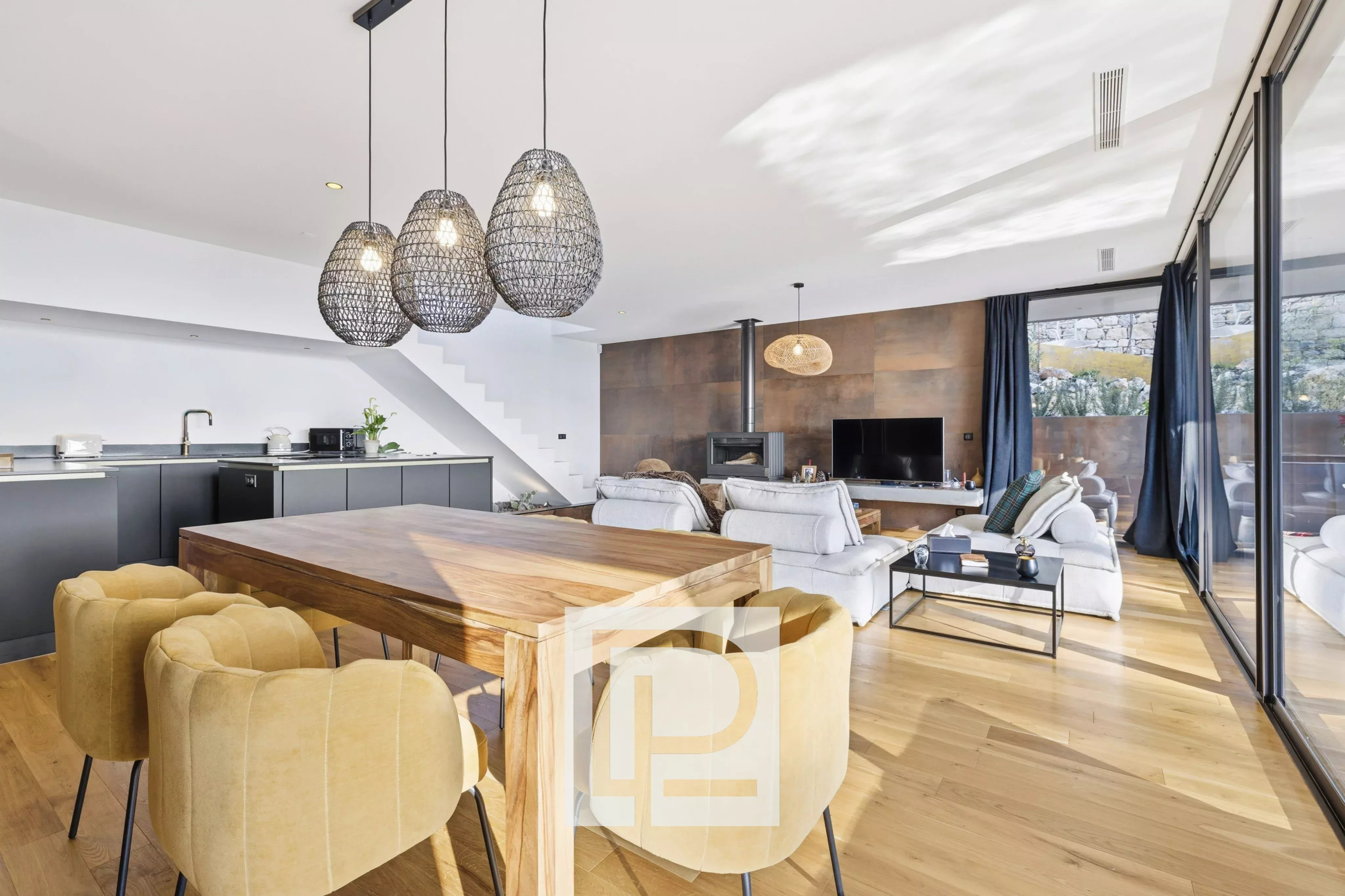 Open-plan living area with a wooden dining table and mustard chairs, grey kitchen cabinets, and a cozy lounge with a fireplace and TV.