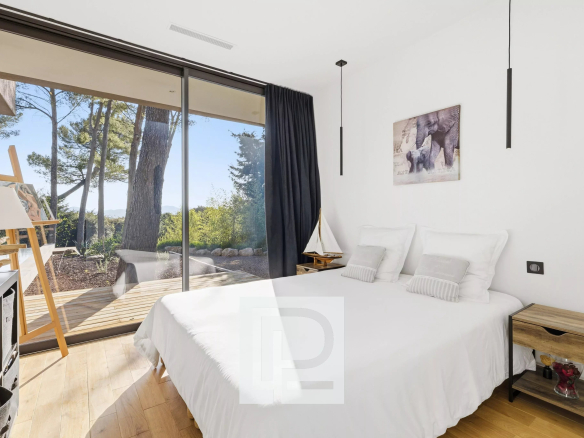 Bright bedroom with a large glass sliding door opening to a wooden deck and garden, white bedding and minimalist decor