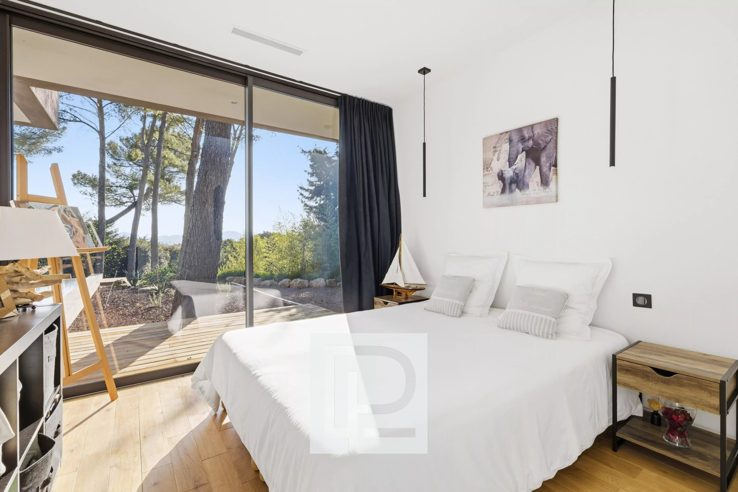 Bright bedroom with a large glass sliding door opening to a wooden deck and garden, white bedding and minimalist decor