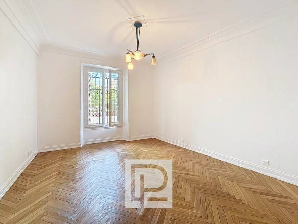 Empty room with white walls, herringbone wood floor, and a window with decorative iron bars.