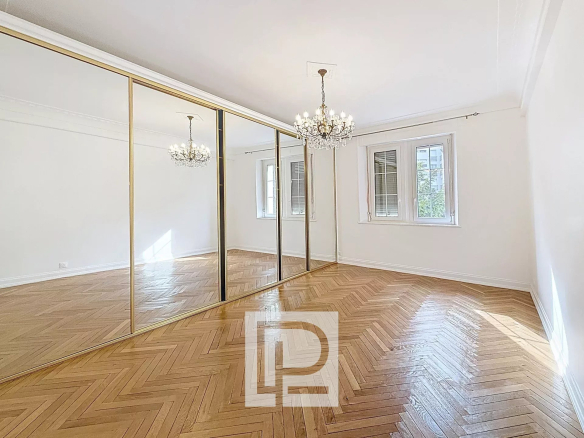 Bright empty room with herringbone wood floor, gold-framed mirrored closets, and a crystal chandelier.