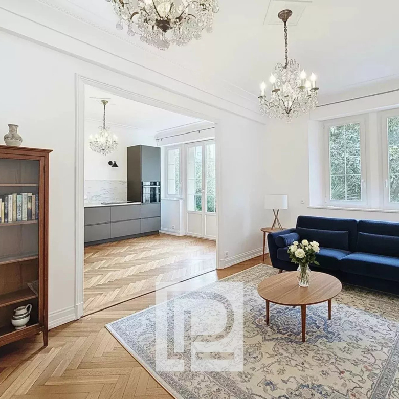 Bright living room with a royal blue sofa, round wooden coffee table, and a patterned rug. Large windows let in natural light; candlestick overhead.