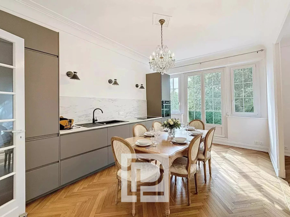 Bright dining area in a modern kitchen with marble backsplash, gray cabinets, and a crystal chandelier overhead.