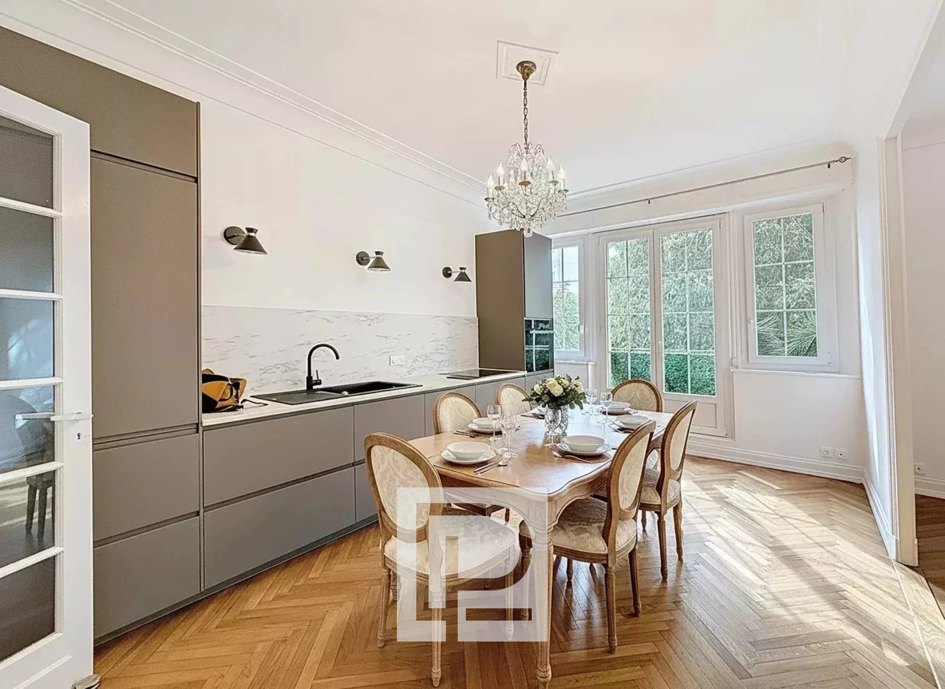 Bright dining area in a modern kitchen with marble backsplash, gray cabinets, and a crystal chandelier overhead.