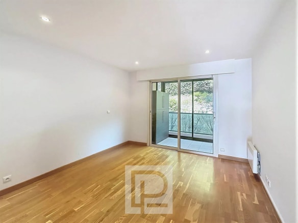 Intérieur d'un appartement vide avec parquet et accès à un balcon.