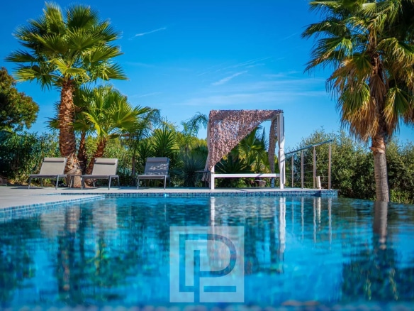 Swimming pool with sun loungers and pergola in a sunny landscaped garden.