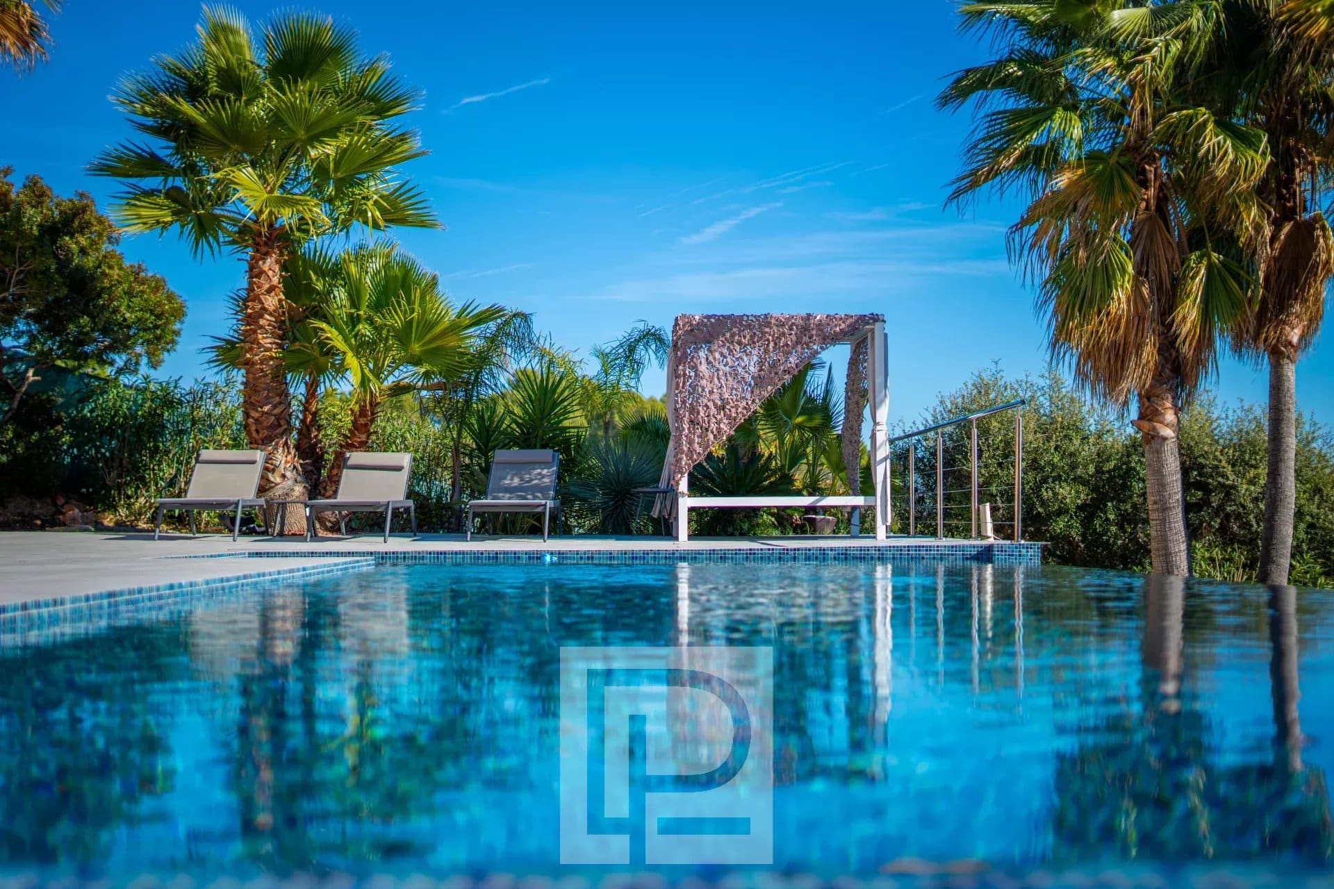 Swimming pool with sun loungers and pergola in a sunny landscaped garden.