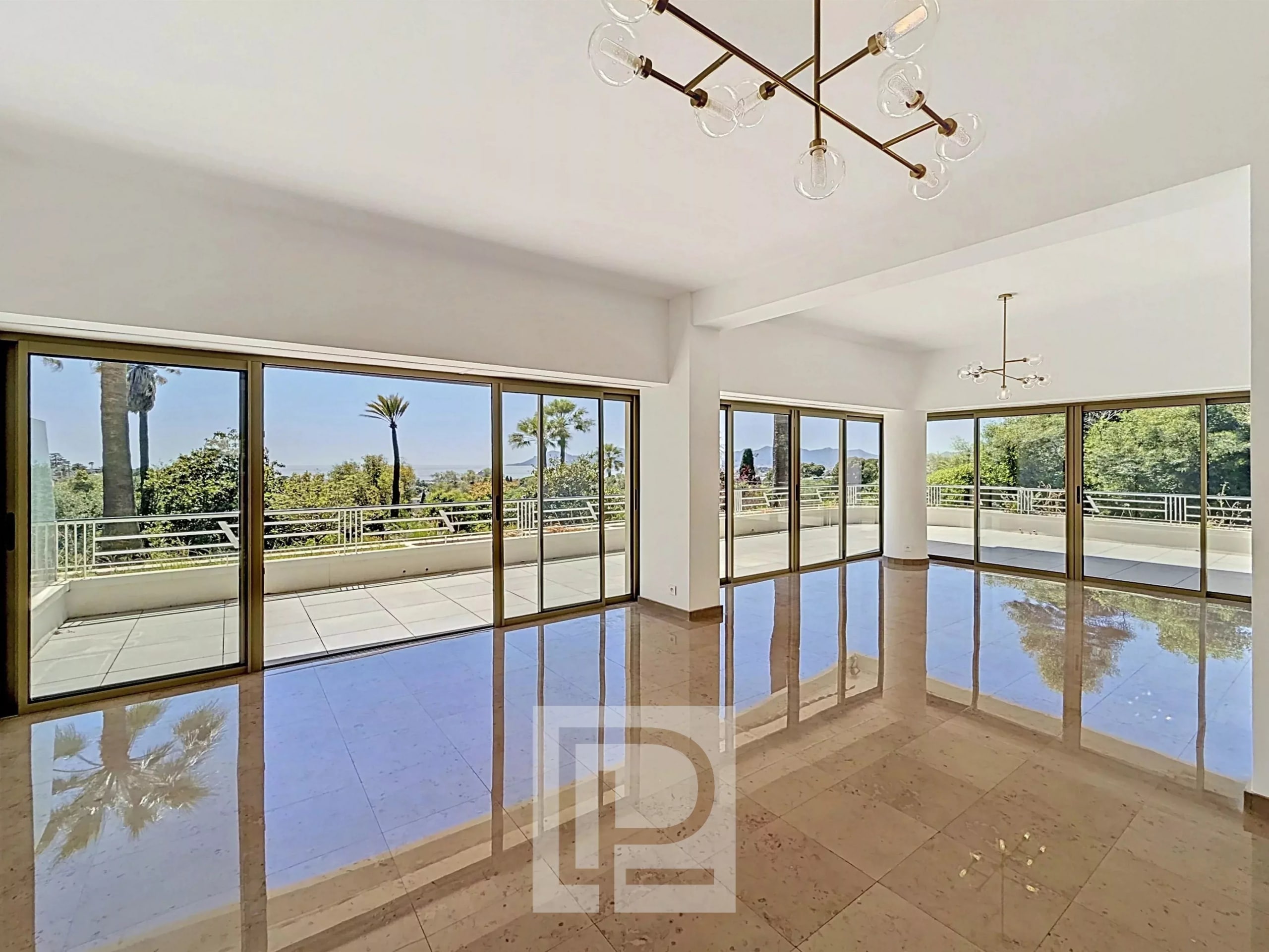 Bright interior of an apartment in Cannes with large bay windows and a view of a park.