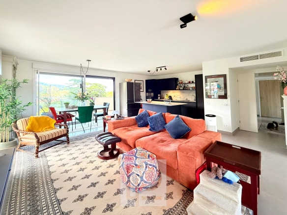 Salon spacieux d'un appartement avec vue sur les collines et la mer, décoré avec un canapé orange et des plantes.