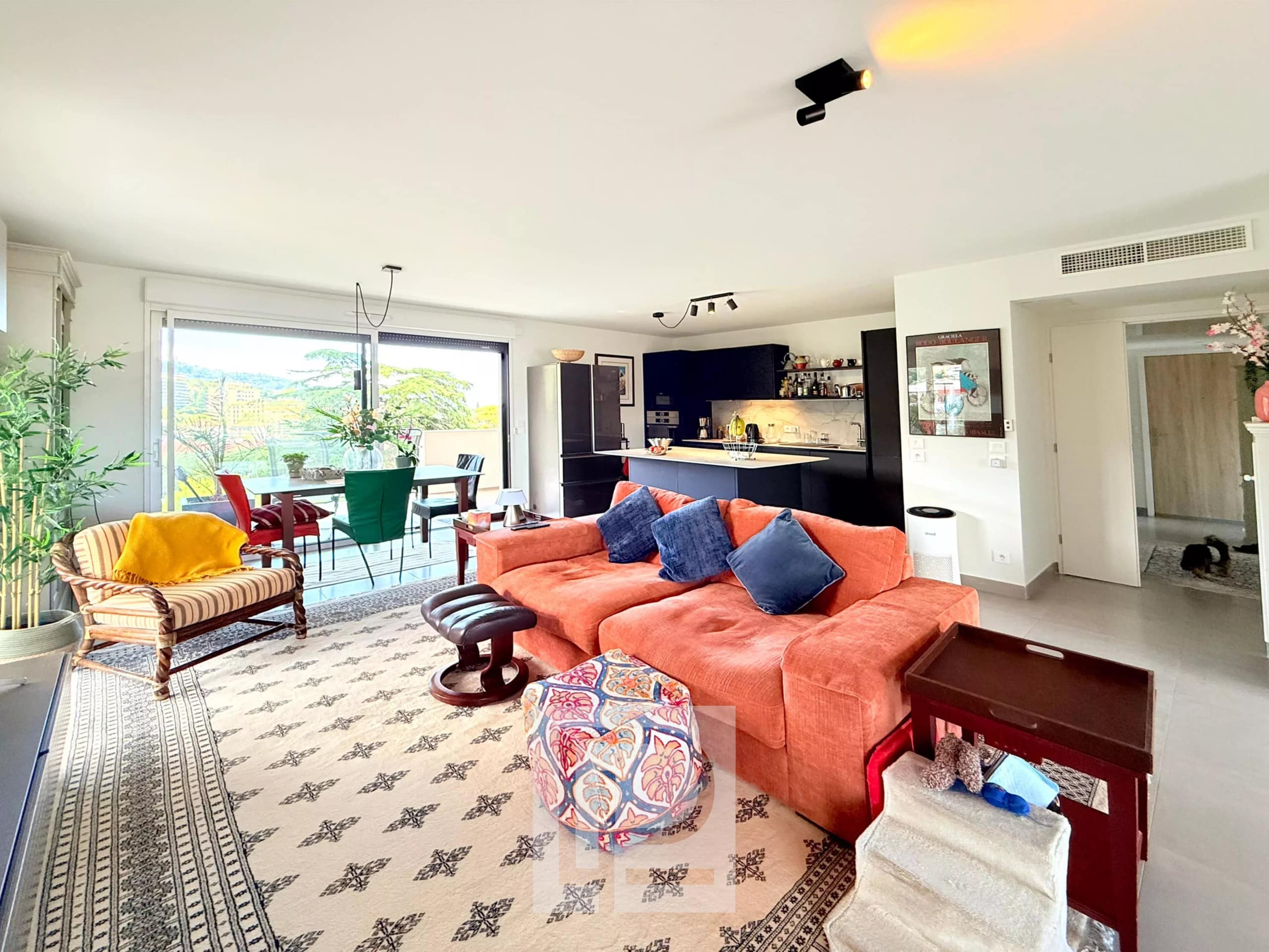 Salon spacieux d'un appartement avec vue sur les collines et la mer, décoré avec un canapé orange et des plantes.