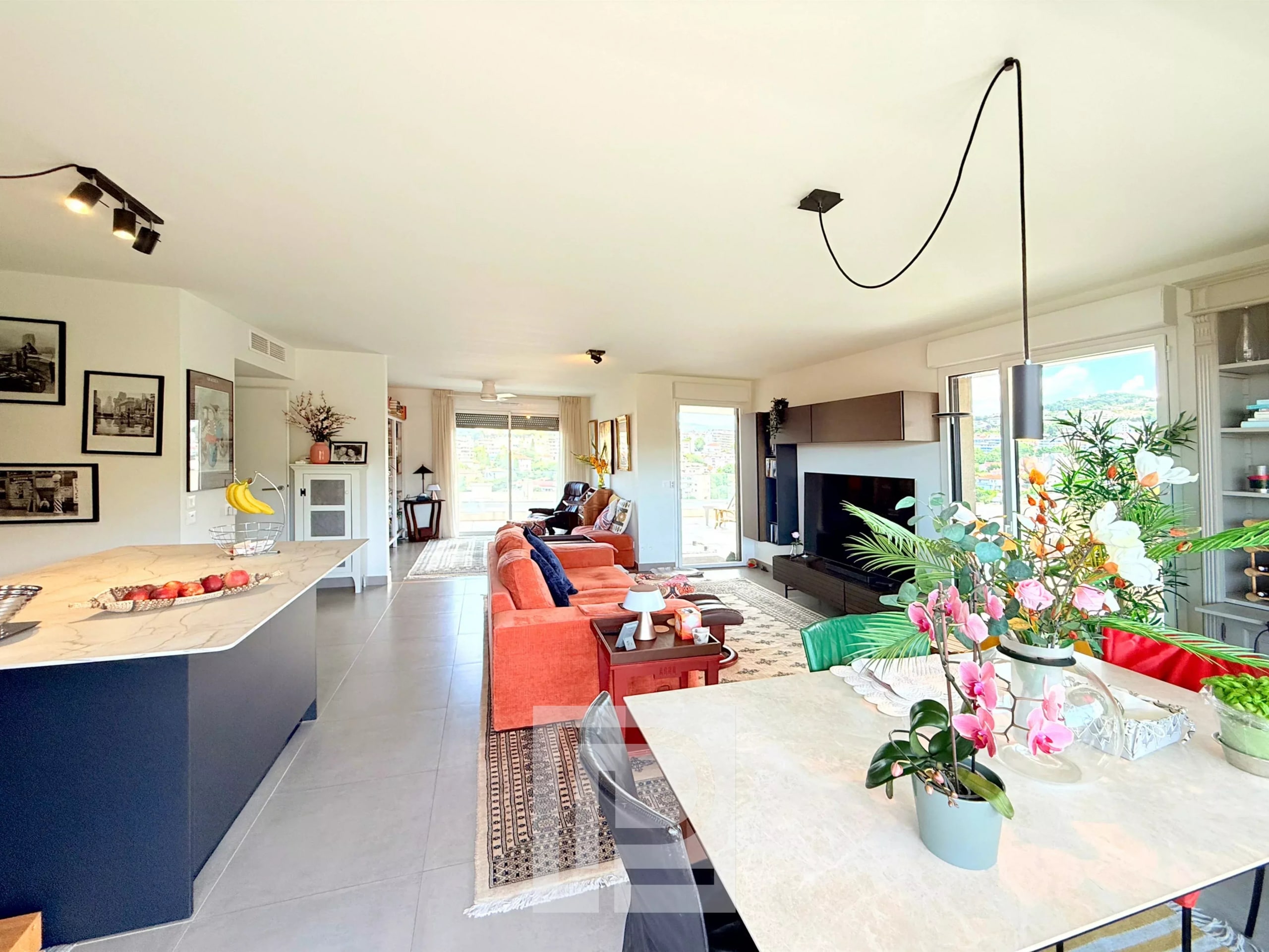 Intérieur d'un appartement moderne avec vue sur les collines et la mer, salon lumineux et cuisine ouverte.