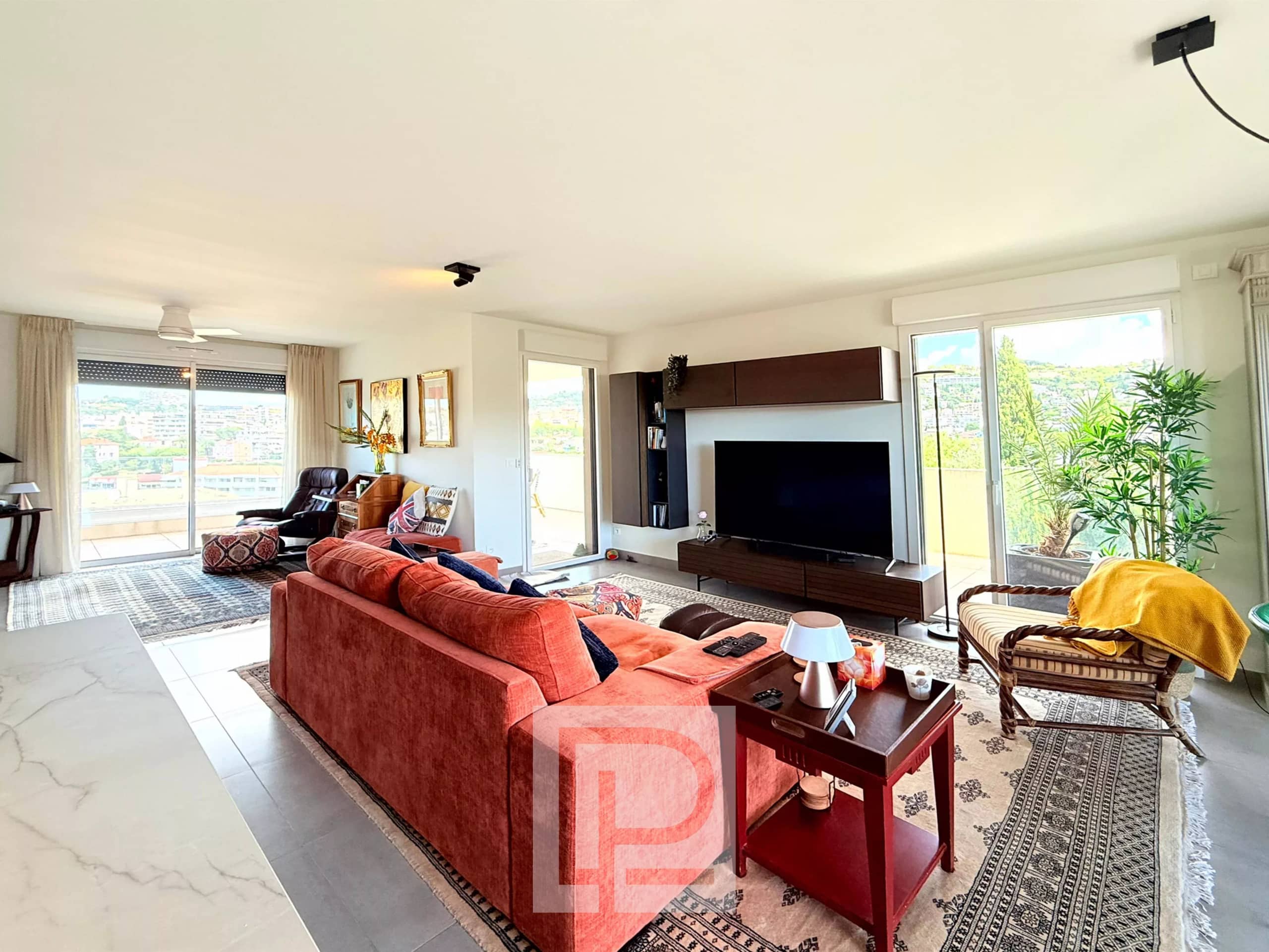 Salon lumineux d'un appartement avec vue sur collines et mer, mobilier moderne et décoration soignée.