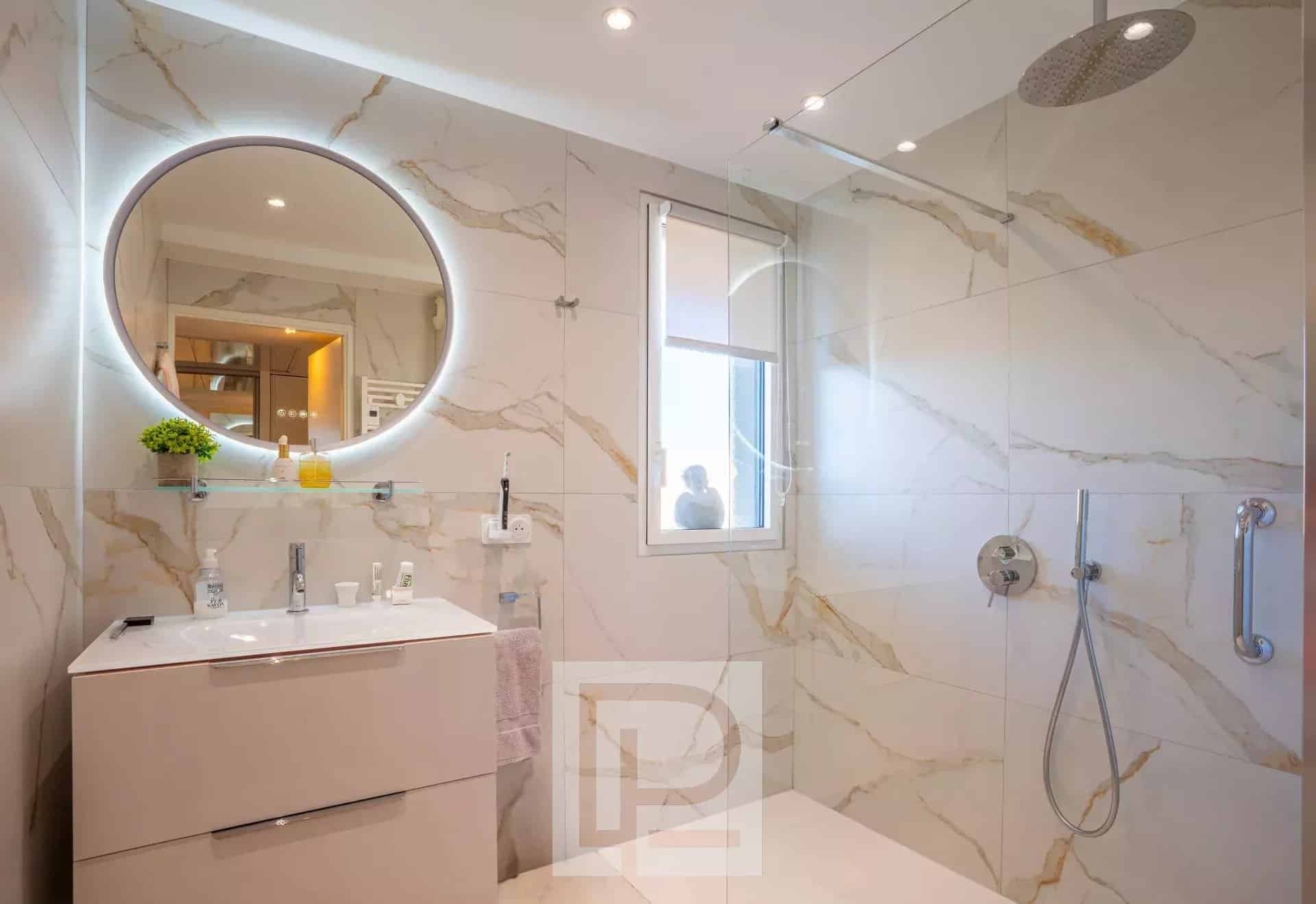 Salle de bain moderne avec douche à l'italienne et miroir rond lumineux.