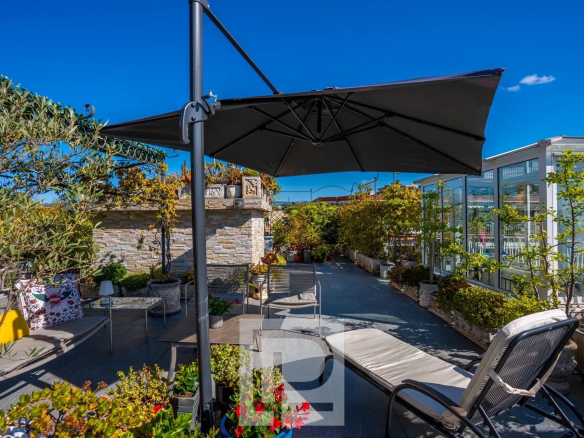 Terrasse panoramique d'un appartement au dernier étage avec mobilier et parasol, vue dégagée.
