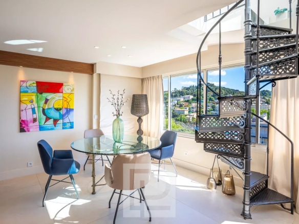 Intérieur d'un appartement rénové avec table ronde et escaliers en colimaçon, vue sur la ville.