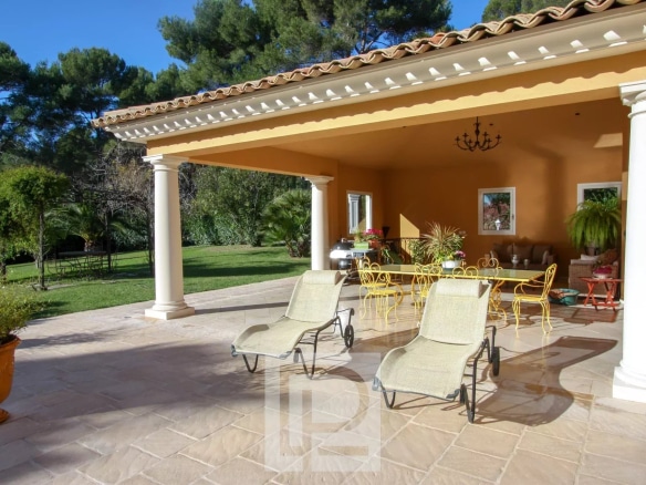 Terrasse d'une villa à Mougins avec chaises longues et vue sur un jardin paysagé.
