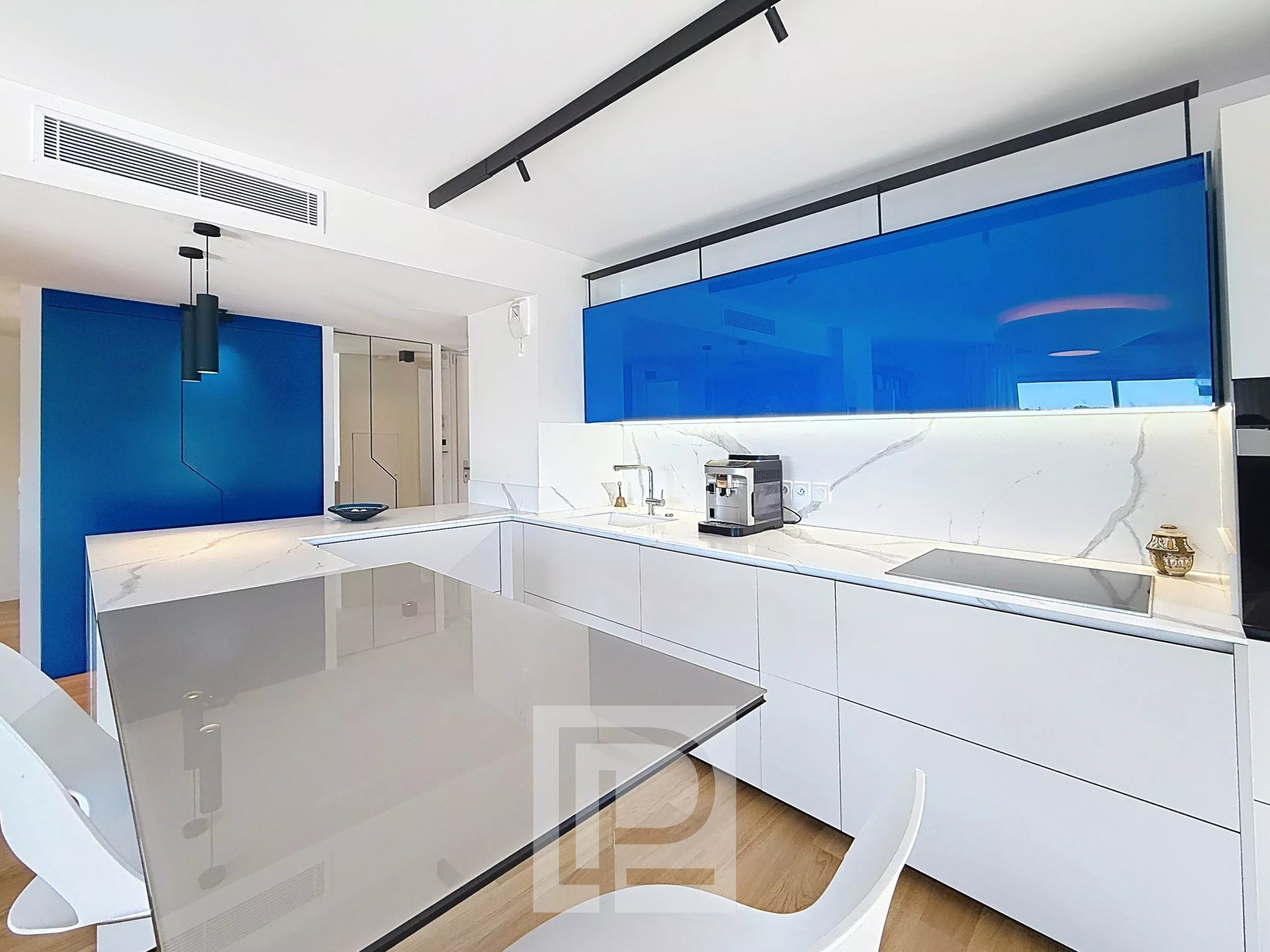 Cuisine moderne d'un appartement avec un plan de travail en verre et des éléments bleus.