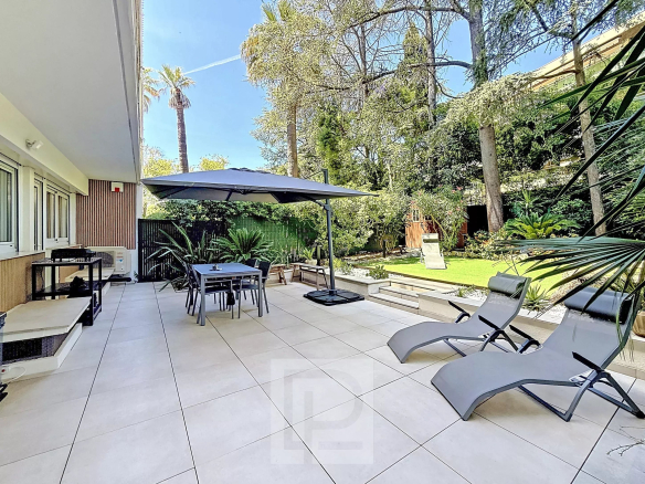 Terrace of a renovated apartment with garden in Cannes, garden furniture and parasol.