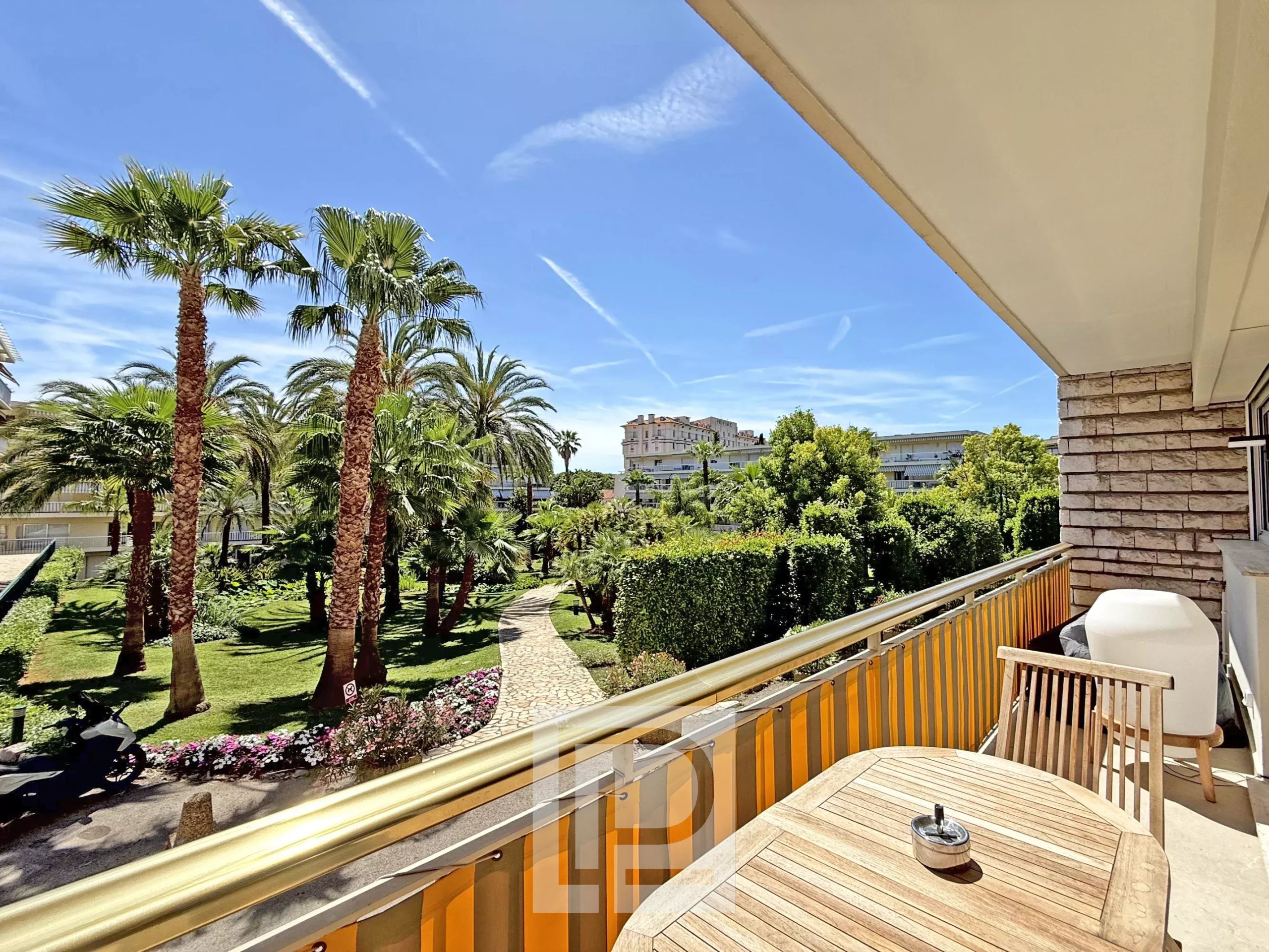 Renovated apartment with garden in Cannes Balcony of a renovated apartment in Cannes overlooking a garden with trees and palm trees.