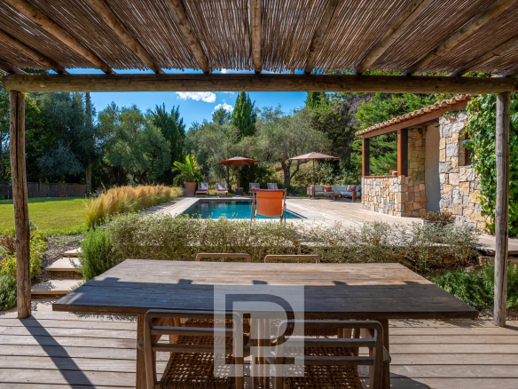 Terrasse en bois avec table, vue sur piscine et jardin verdoyant, bastide rénovée à Pégomas.