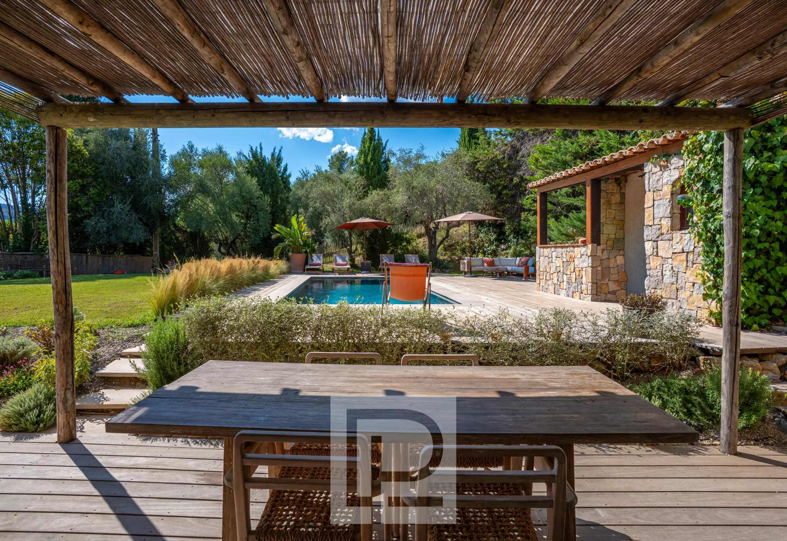 Bastide rénovée avec vue sur piscine Terrasse en bois avec table, vue sur piscine et jardin verdoyant, bastide rénovée à Pégomas.