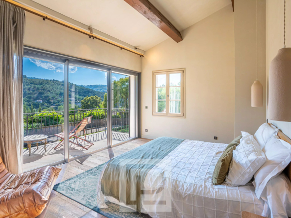 Chambre lumineuse avec vue sur les collines, fenêtres ouvertes sur un balcon.