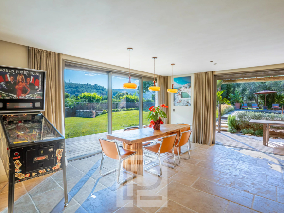 Intérieur d'une bastide rénovée avec vue sur la nature, table en bois et machine à flipper.