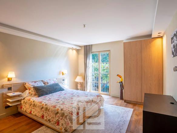 Chambre d'une bastide rénovée avec lit floral et fenêtre donnant sur un environnement bucolique.