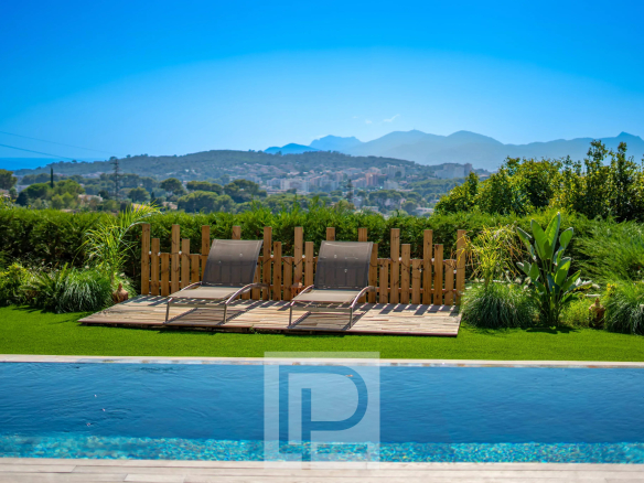 Vue sur la piscine et les chaises longues dans un jardin avec collines en arrière-plan.