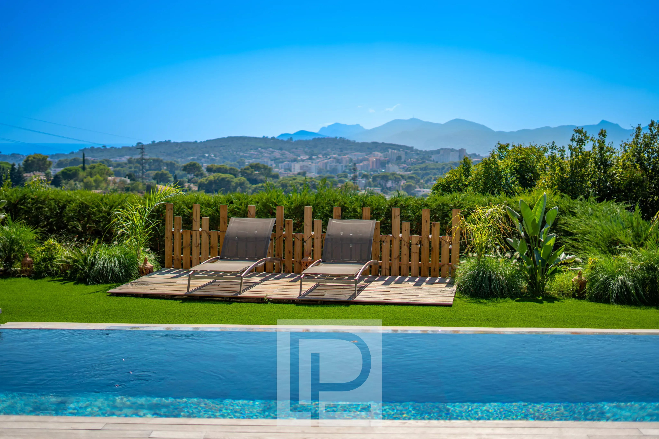 Vue sur la piscine et les chaises longues dans un jardin avec collines en arrière-plan.