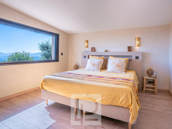 Chambre d'une villa rénovée avec vue sur la mer à Mougins, murs clairs et lit double.