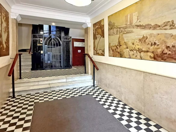 Hall d'entrée d'une résidence emblématique des années 30 à Cannes, avec sol en damier et fresques murales.