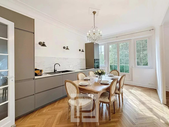 Cuisine élégante d'un appartement rénové avec table à manger et fenêtres donnant sur un jardin.