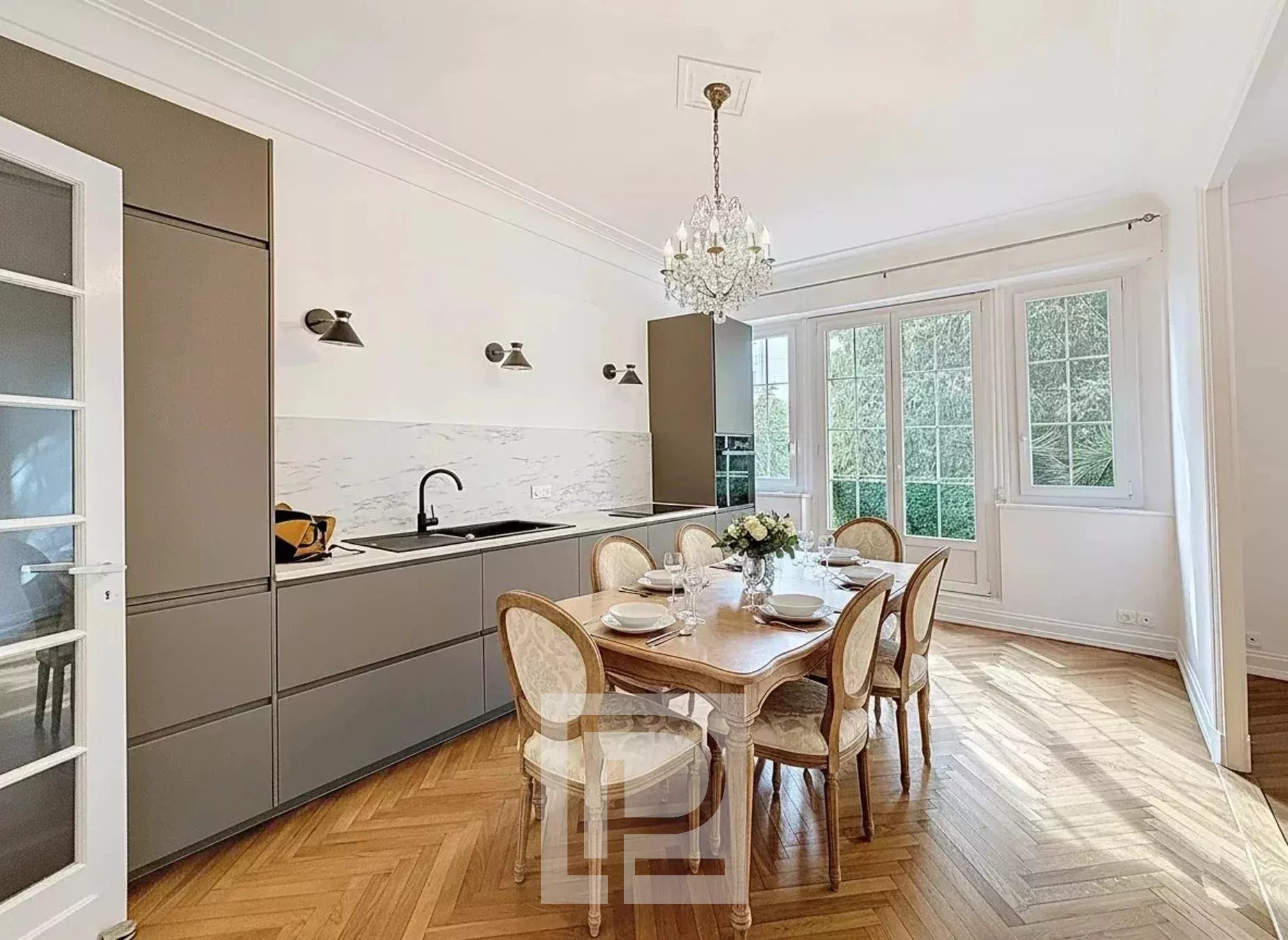 Cuisine d’un appartement bourgeois à Cannes Cuisine élégante d'un appartement rénové avec table à manger et fenêtres donnant sur un jardin.