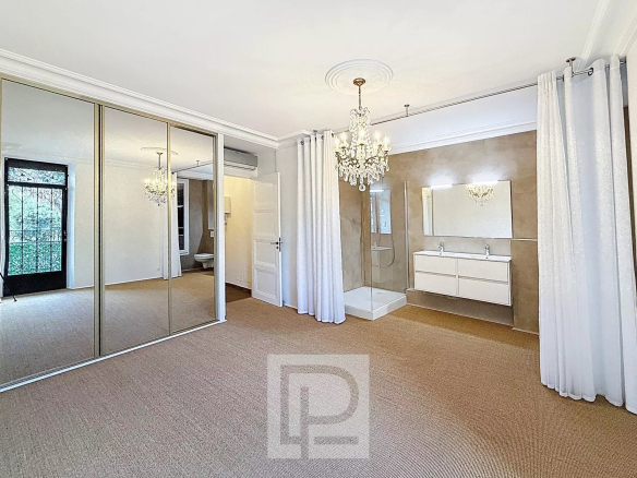 Chambre spacieuse avec miroir, lustre et salle de bain dans un appartement à Cannes.