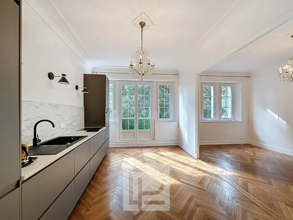 Cuisine moderne et salon lumineux d'un appartement rénové à Cannes, avec parquet et fenêtres donnant sur un jardin.