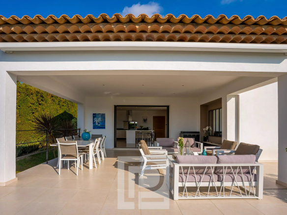 Terrasse couverte d'une villa californienne à Mougins, avec mobilier moderne et vue sur la nature.