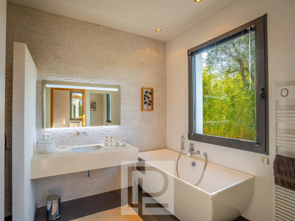 Salle de bain moderne avec baignoire et miroir, lumière naturelle à travers la fenêtre.