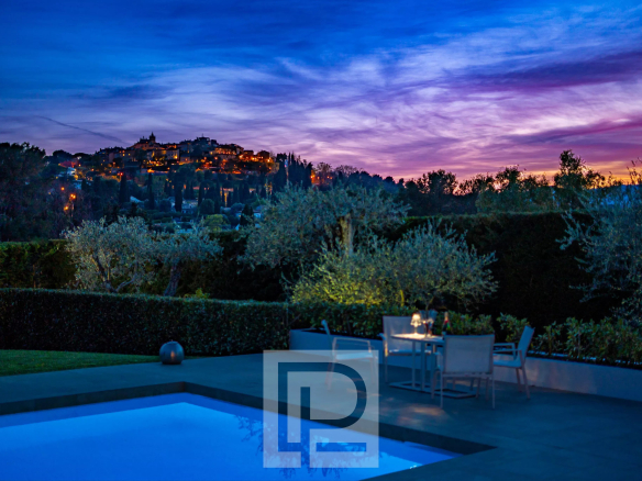 Vue d'une villa avec piscine au crépuscule, surplombant un village historique à Mougins.